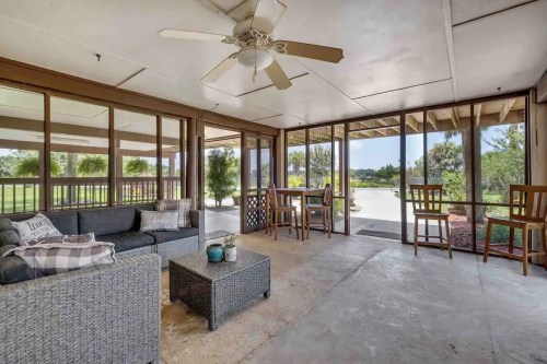 A screened porch with a sofa, coffee table, and bar stools, overlooking a green outdoor area.