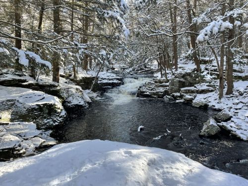 A serene winter scene featuring a flowing river surrounded by snow-covered rocks and trees.
