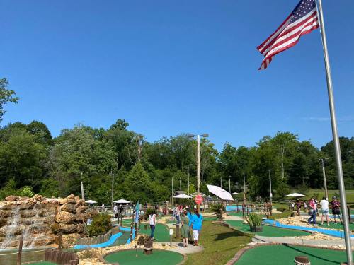 A mini-golf course with players, a waterfall, and an American flag waving in a clear blue sky.