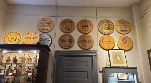 A wall display featuring wooden barrel heads from various distilleries and a glass cabinet with bottles.