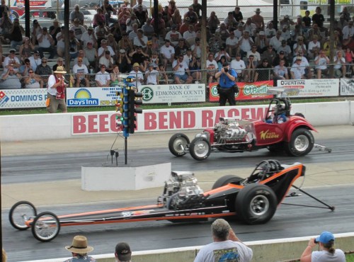 Two drag racing cars compete on a track, with a crowd watching in the background at Beech Bend Raceway.