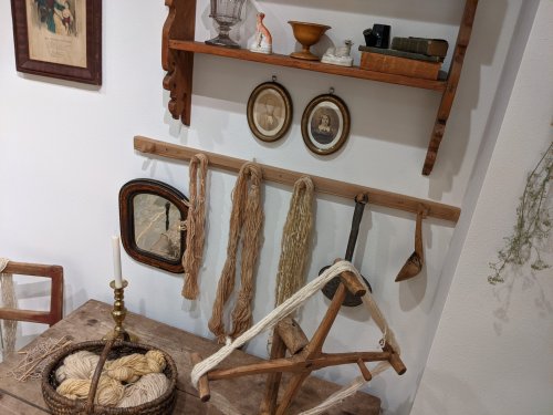 A rustic display featuring yarn, wooden tools, and framed pictures on a wall shelf above a wooden table.