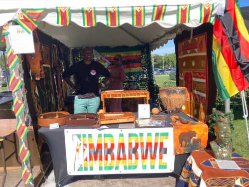 A vibrant booth showcasing Zimbabwean culture, featuring crafts, textiles, and a smiling vendor.