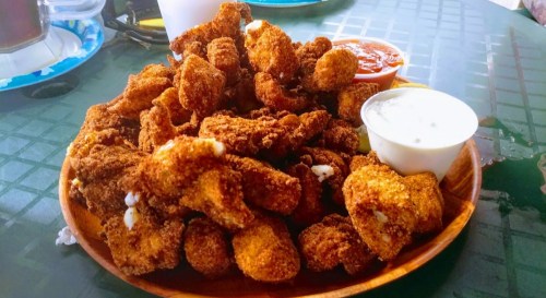 A wooden plate piled high with golden-brown fried food, accompanied by dipping sauces.