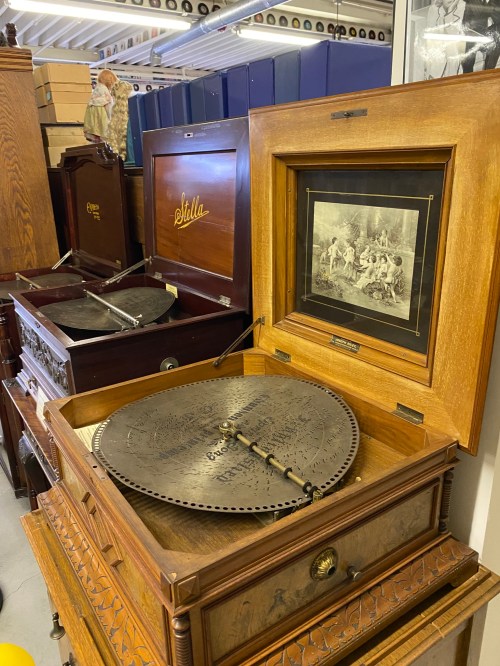 An antique music box with a large metal disc, displayed in a collection of vintage furniture and decor.