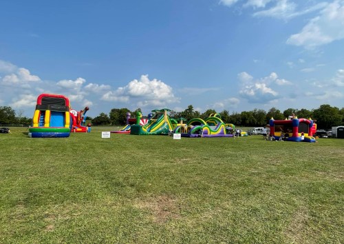 A sunny outdoor scene featuring colorful inflatable bounce houses and slides on a grassy field.