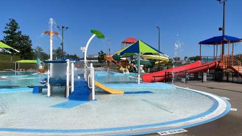 A colorful water park featuring slides, splash pads, and water features under clear blue skies.