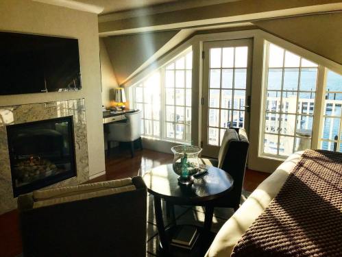 Cozy living space with a fireplace, large windows, and a view of the water, featuring modern furniture and warm lighting.