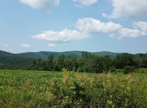 A scenic view of rolling hills and a green field under a partly cloudy sky.