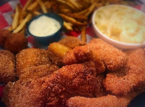 A plate of crispy fried food, including fish, fries, and macaroni and cheese, served with a dipping sauce.