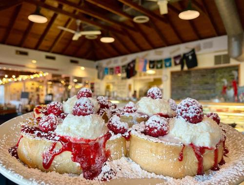 A plate of sweet rolls topped with whipped cream, raspberry sauce, and fresh raspberries, dusted with powdered sugar.