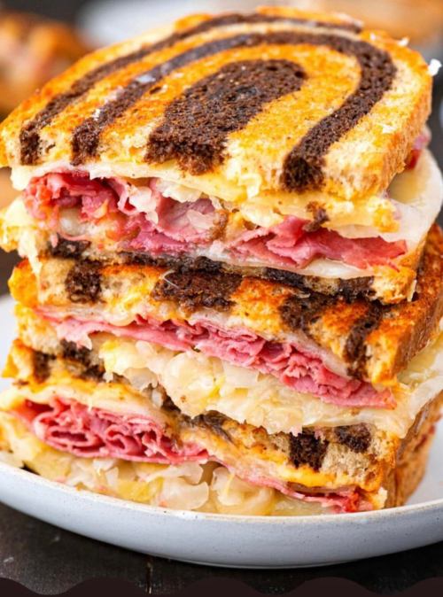 A stack of grilled sandwiches with layers of corned beef, sauerkraut, and melted cheese on marbled rye bread.