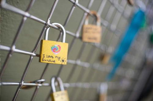 A colorful padlock with "I love my sunshine" written on it, attached to a metal fence among other locks.