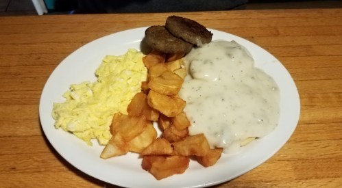 A plate of scrambled eggs, sausage patties, and crispy fried potatoes topped with creamy gravy.