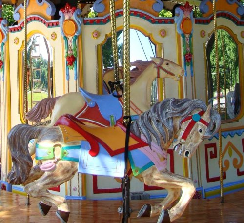 Colorful carousel horses with intricate designs, set against a vibrant, mirrored backdrop.
