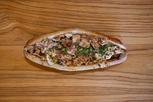 A toasted sandwich filled with shredded meat and herbs, served on a wooden surface.