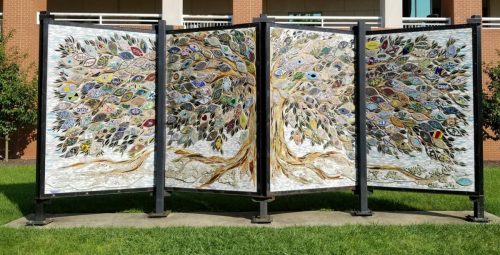 A large, decorative tree sculpture made of colorful tiles, set in a grassy area near a building.