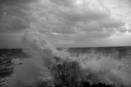 A dramatic black and white image of crashing ocean waves under a cloudy sky.