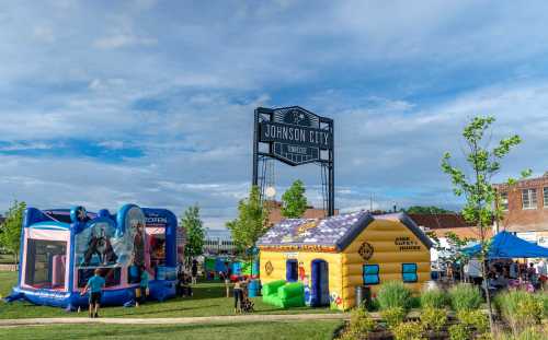 Colorful bounce houses and a sign for Johnson City under a blue sky, with people enjoying a community event.