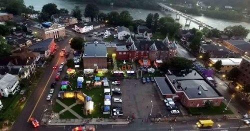 Aerial view of a vibrant community event with tents, food trucks, and a river in the background.