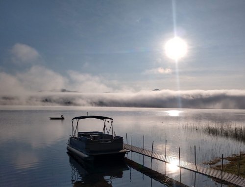 A serene lake at sunrise, with mist over the water and a small boat near a dock.