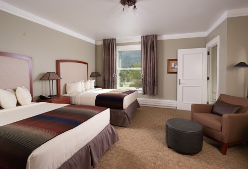 A cozy hotel room featuring two beds, a chair, and large windows with natural light.