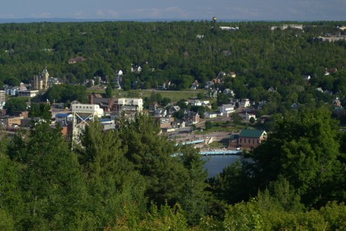 A scenic view of a small town surrounded by lush greenery and a river, with buildings and trees in the foreground.