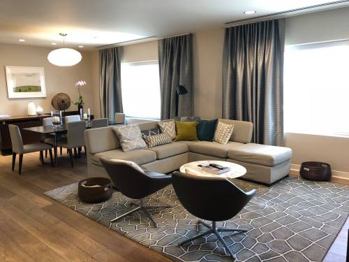 A modern living room featuring a sectional sofa, two chairs, a coffee table, and a dining area with a large window.