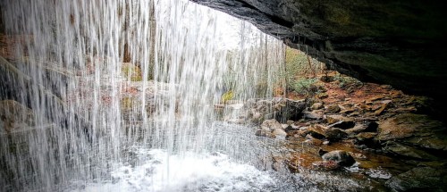 A serene waterfall cascades over rocks, surrounded by trees and a tranquil pool below.