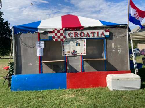 A colorful tent with a sign reading "CROATIA," featuring red, white, and blue colors, set up in a grassy area.