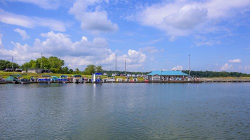 A serene waterfront scene with boats docked at a marina under a blue sky with fluffy clouds.