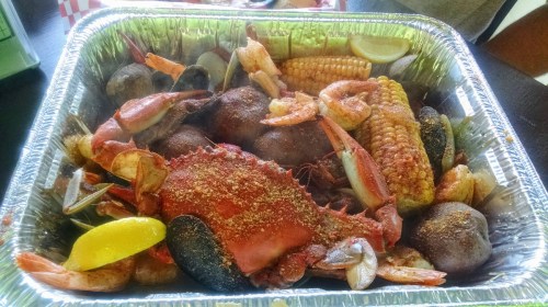A seafood feast in a tray, featuring crab, shrimp, corn, and potatoes, garnished with lemon slices.