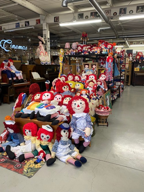 A collection of numerous rag dolls with red hair displayed in a vintage shop, creating a colorful and nostalgic scene.