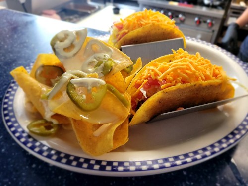 A plate of tacos with shredded cheese, jalapeños, and a side of nachos topped with sour cream and jalapeños.