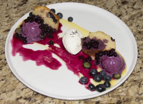 A dessert plate featuring blueberry cake, berry sorbet, and a scoop of vanilla ice cream, drizzled with berry sauce.