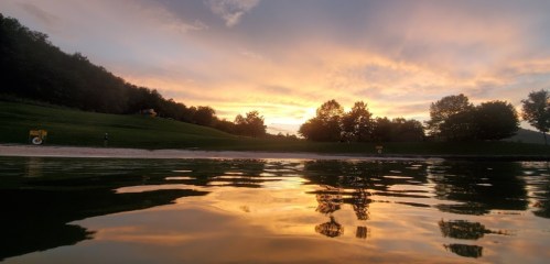A serene sunset over a calm lake, with vibrant colors reflecting on the water's surface and trees in the background.