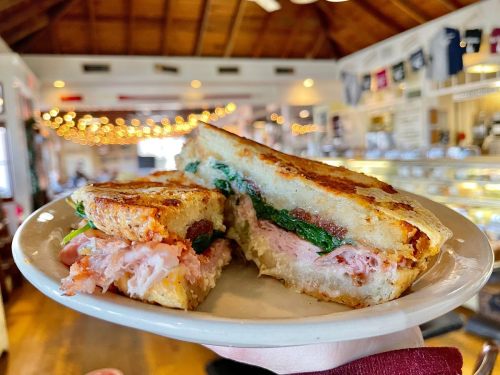 A hand holding a plate with a grilled sandwich filled with ham and spinach, set in a cozy, warmly lit café.