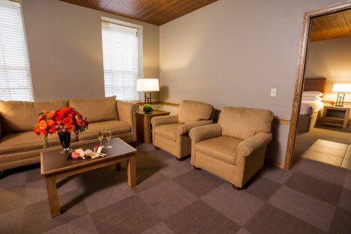 Cozy hotel room with a sofa, two armchairs, a coffee table, and a bouquet of flowers. Soft lighting and warm decor.