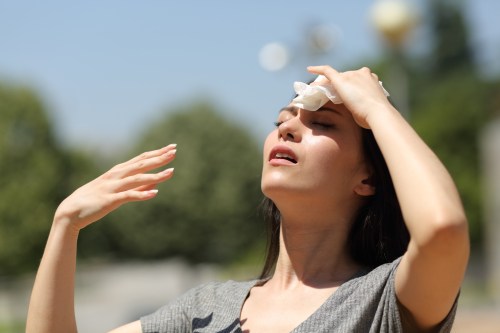 A woman wipes her forehead with a cloth, looking up and squinting in bright sunlight.