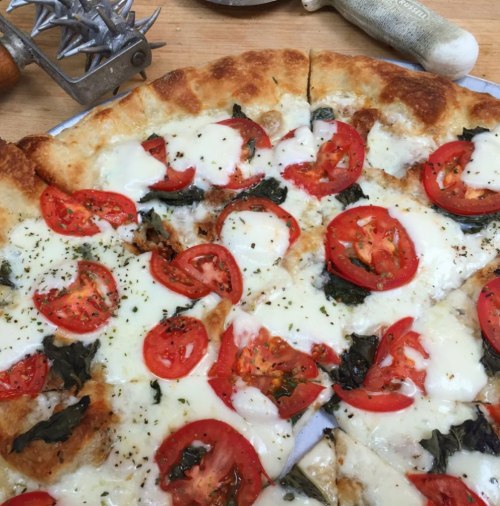 A freshly baked pizza topped with mozzarella, sliced tomatoes, and fresh basil on a golden crust.