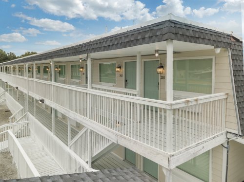 A two-story motel with white railings and doors, featuring outdoor balconies and a clear blue sky in the background.