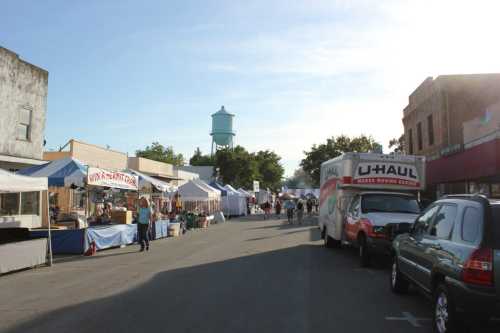 A street lined with vendor tents and a U-Haul truck, with a water tower in the background under a clear sky.