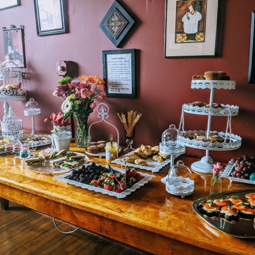 A beautifully arranged dessert table with various pastries, fruits, and flowers against a warm-colored wall.