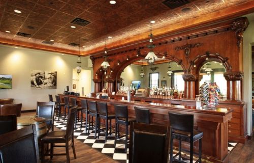 Elegant bar interior with wooden accents, high stools, and a checkered floor, featuring a variety of drinks on display.