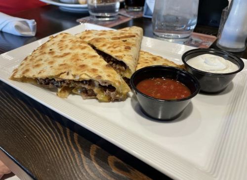 A plate of quesadillas filled with black beans and cheese, served with salsa and sour cream on the side.