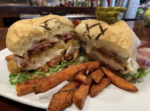 A close-up of a sandwich with chicken, bacon, and lettuce, served with sweet potato fries on a plate.
