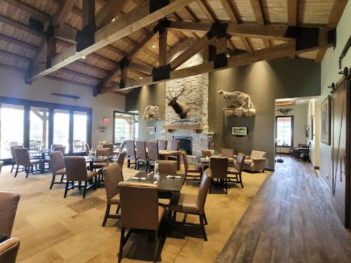 A spacious restaurant interior with wooden beams, stone fireplace, and rustic decor featuring animal mounts.