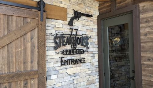 Sign for "77 Steakhouse & Saloon" with a gun decoration, located at the entrance of a rustic building.