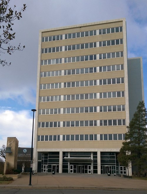 A tall, modern building with multiple windows, featuring a sign for the county courthouse and a cloudy sky above.
