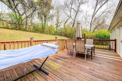 A wooden deck with a hammock, patio table, and chairs, surrounded by trees and greenery.